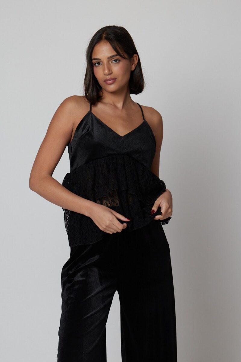 Mujer con top negro satinado con volantes de encaje, estilo casual elegante.